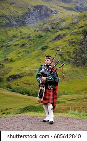 SCOTTISH HIGHLANDS - SEPTEMBER 24, 2015: Piper in traditional Scottish outfit plays on bagpipes in Scottish Highlands. In the background of the mountain. Cloudy autumn day.
