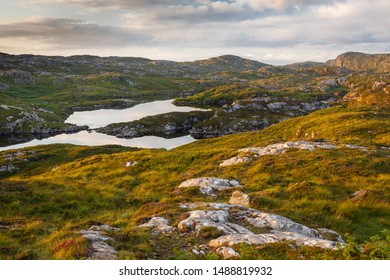 Scottish Highlands with small lakes and rocky mountains full of biting midges, lit by late sunset