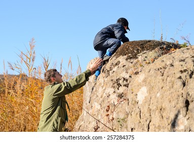 Scout Helping A Young Boy Rock Climbing Giving Him A Helping Hand From Below As He Learns About The Wilderness And Nature