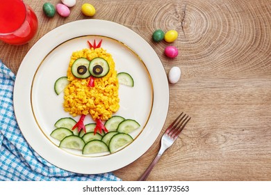 Scrambled egg easter chick made it from scrambled eggs,cucumbers,black olives and red hot peppers on plate with wooden background.Art food idea for kids Easter's breakfast.Top view.Copy space