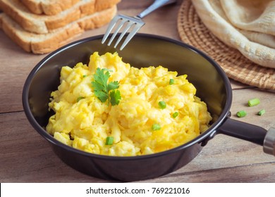Scrambled egg in frying pan and toast on wooden table
