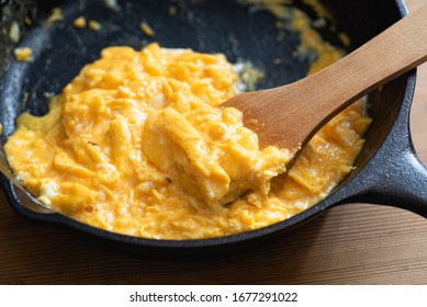 Scrambled Eggs Cooked In An Cast Iron Skillet, Wooden Spatula.