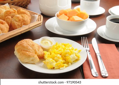 Scrambled eggs, a croissant and a bowl of cantalope for breakfast