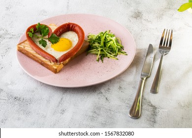 Scrambled eggs in the form of heart on a white plate with sausages, sourdough toast isolated on white marble background. Homemade food. Tasty breakfast. Selective focus. Hotizontal photo.