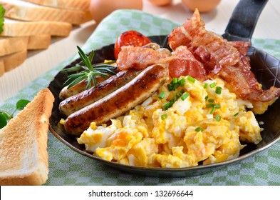 Scrambled eggs with fried bacon, fried sausages, grilled tomato and toast