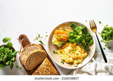 Scrambled Eggs, Sandwich With Cream Cheese And Salmon And Salad Leaves At White Stone Table. Nordic Diet. Top View With Copy Space.