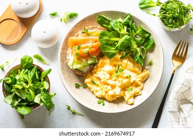 Scrambled Eggs, Sandwich With Cream Cheese And Salmon And Salad Leaves At White Stone Table.