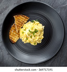 Scrambled Eggs With Toast On Black Plate. Overhead View.