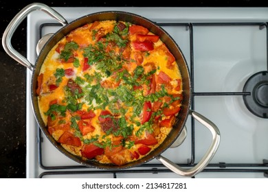 Scrambled Eggs With Vegetables And Herbs In Black Frying Pan On White Stove. Top View