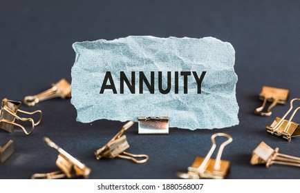 A Scrap Of Blue Paper With Clips On A Gray Background With The Text - ANNUITY. Conceptual Photo Fixed Sum Of Money Paid To Someone Each Year Floor.