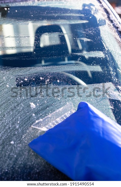 Scraping ice from frosted car window early in sunny
morning 