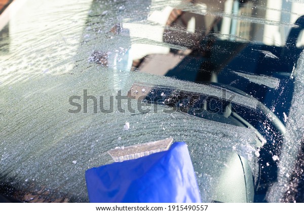 Scraping ice from frosted car window early in sunny\
morning 