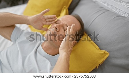 Scratching eyes indoors, middle-aged man's morning saga on his cozy bed, inside a comfortable bedroom, balancing relaxation  concentration amid pajama rest