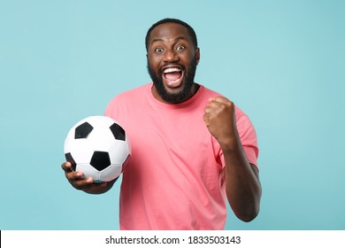 Screaming african american man football fan in pink t-shirt isolated on blue background. Sport family leisure lifestyle concept. Cheer up support favorite team with soccer ball, doing winner gesture