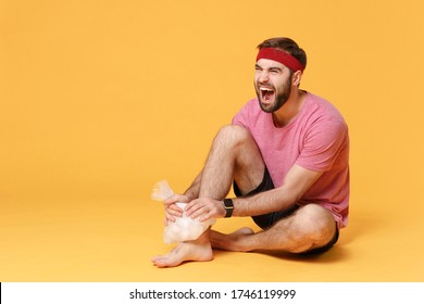 Screaming Bearded Fitness Sporty Guy Sportsman In Headband T-shirt In Home Gym Isolated On Yellow Background. Workout Sport Motivation Concept. Get Injured Hold Ice Pack Cooling Down Ankle Foot Pain