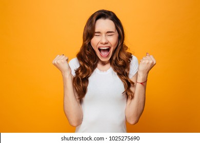Screaming brunette woman in t-shirt with closed eyes and open mouth over yellow background