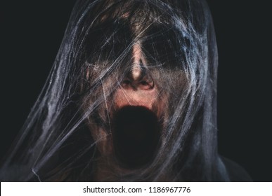 Screaming creepy character covered with spiderweb on black background. Halloween spooky creature portrait with copy space