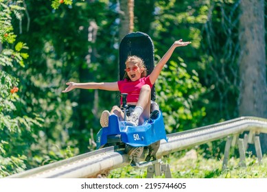 Screaming girl riding mountain roller coaster with outstretched arms. Forest in background - Powered by Shutterstock