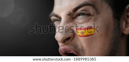 A screaming man with the image of the Spain national flag on his face.