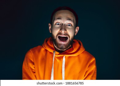 Screaming. Portrait Of Crazy Scared And Shocked Caucasian Man Isolated On Dark Background. Copyspace For Ad. Bright Facial Expression, Human Emotions Concept. Watching Horror On TV, Cinema.