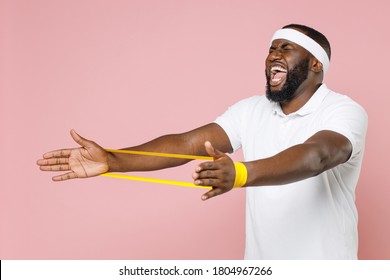 Screaming Tired Young Bearded African American Fitness Sports Man 20s In Headband T-shirt Doing Exercise With Fitness Gums Spend Time In Gym Isolated On Pastel Pink Color Background Studio Portrait