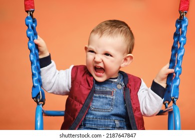 Screaming Toddler Baby Boy Rides On A Swing. A Frightened Child Swings On The Playground, Kid Aged One Year