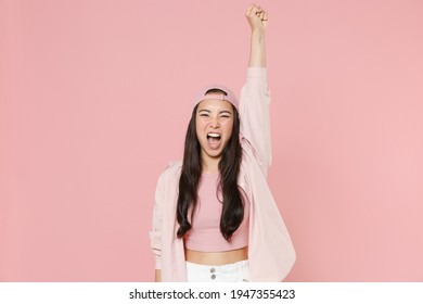 Screaming young asian woman girl in casual clothes cap posing isolated on pastel pink background studio portrait. People emotions lifestyle concept. Mock up copy space. Rising hand clenching fist
