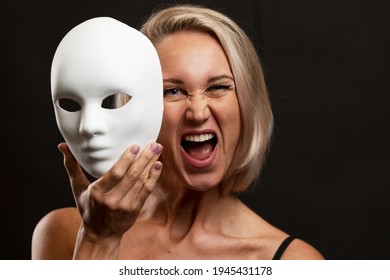 Screaming Young Blonde Woman With A White Mime Mask In Her Hand. Change Of Amotions. Black Background.