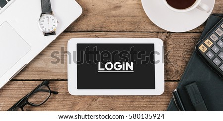 Screen with Login text on tablet, Office desk with electronic devices, computer and paper, wood table from above, concept image for blog title or header image.