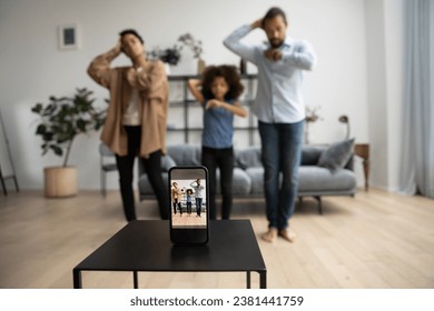 Screen of smartphone recording happy young Black parents and kid dancing together at home, broadcasting online, shooting videofor family personal blog, vlog. Cellphone close up with blurred dancers - Powered by Shutterstock