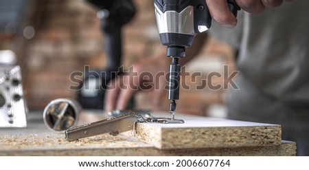 Screwing a self-tapping screw into a metal fastening hole on a wood strip using a screwdriver, the work of a carpenter.