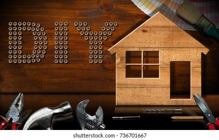 Screws in the shape of text Diy (Do it yourself), wooden model house with work tools on a desk with reflections. Home improvement concept