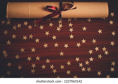 Scroll of paper with brown ribbon and lots of small gold star confetti on the wooden table background top view flat lay. Magical brown toned christmas backdrop - Powered by Shutterstock