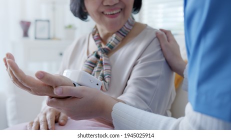 Scrub Nurse Doctor Using Digital Tonometer Check Blood Pressure For Old Asia Female At Home In Elderly Care Cardiovascular Medical Visit, Cholesterol Problem And Hospice Healthcare Caregiver Concept.