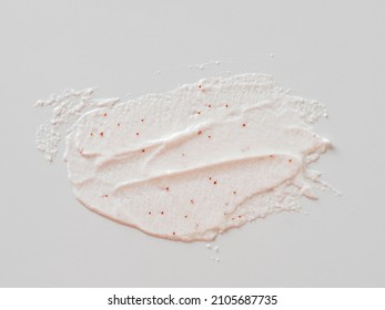 Scrub smears isolated on white background. Texture cosmetic scrub for face and body with red abrasive particles in pastel pink color. Exfoliating body polish texture as cosmetic gommage background