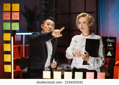 Scrum Kanban Glass Board. Multiethnic Creative Two Diverse Business Colleagues Brainstorm On Work Plan In Office. Korean Man Pointing On Financial Chart On Glass Board Talking With Female Colleague