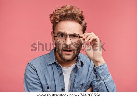 Scrupulous stylish man in denim shirt and spectacles looks with shocked and stupefied expression, tries understand what is written. Strict professor listens to student`s answer, being in stupor