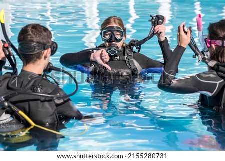 Scuba dive training in the pool with an instructor and two students showing the descent sign