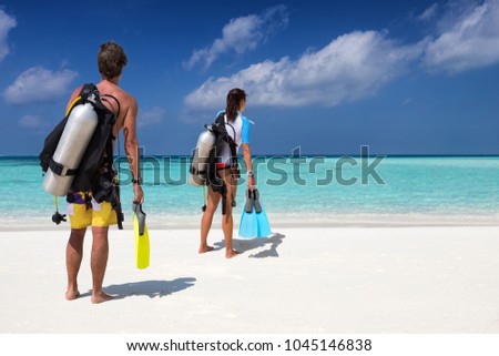 Scuba diver couple with diving equipment on a tropical beach watches the scene