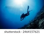 Scuba diver diving towards sun and boat on background underwater