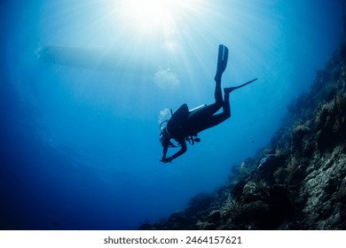 Scuba diver diving towards sun and boat on background underwater