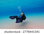 Scuba diver exploring shallow sandy seascape in the vivid blue clear sea. Underwater photography from the scuba diving activity. Tropical seascape, travel photo. Shallow sea and swimming diver.