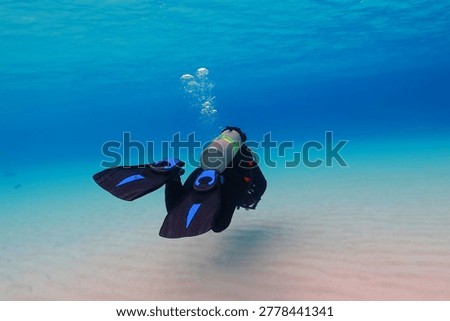 Scuba diver exploring shallow sandy seascape in the vivid blue clear sea. Underwater photography from the scuba diving activity. Tropical seascape, travel photo. Shallow sea and swimming diver.