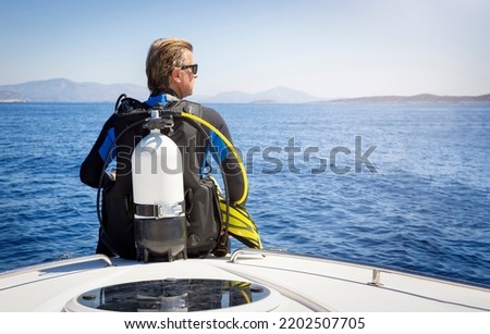 A scuba diver in his diving gear sits in front of a boat and gets ready to go into the sea