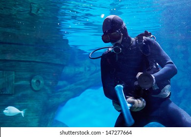 Scuba diver underwater near to sunken sailing ship in oceanarium with suction cup and brush for cleaning glass