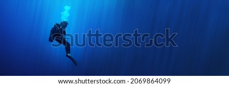 Scuba diver woman standing still in deep blue with sun rays. Can be used as a background for a banner