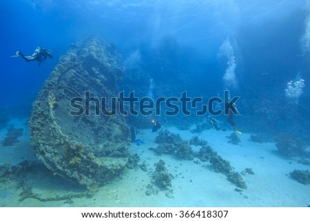 Scuba divers explore a shipwreck in the Red Sea, surrounded by coral reefs and marine life. A stunning underwater scene perfect for adventure and diving enthusiasts.