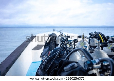 Scuba tanks are in the sharp foreground ready on a dive boat. In the background you can see the out of focus horizon, the sea and the cloudy sky as copy space