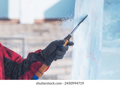 A sculptor processes a large ice cube with a sharp hand tool. Ice dust and ice fragments in the air. Ice sculpture festival in the city.