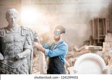 Sculptor In Protective Workware Grinding Stone Sculpture With Electirc Grinder In The Old Studio With Dust